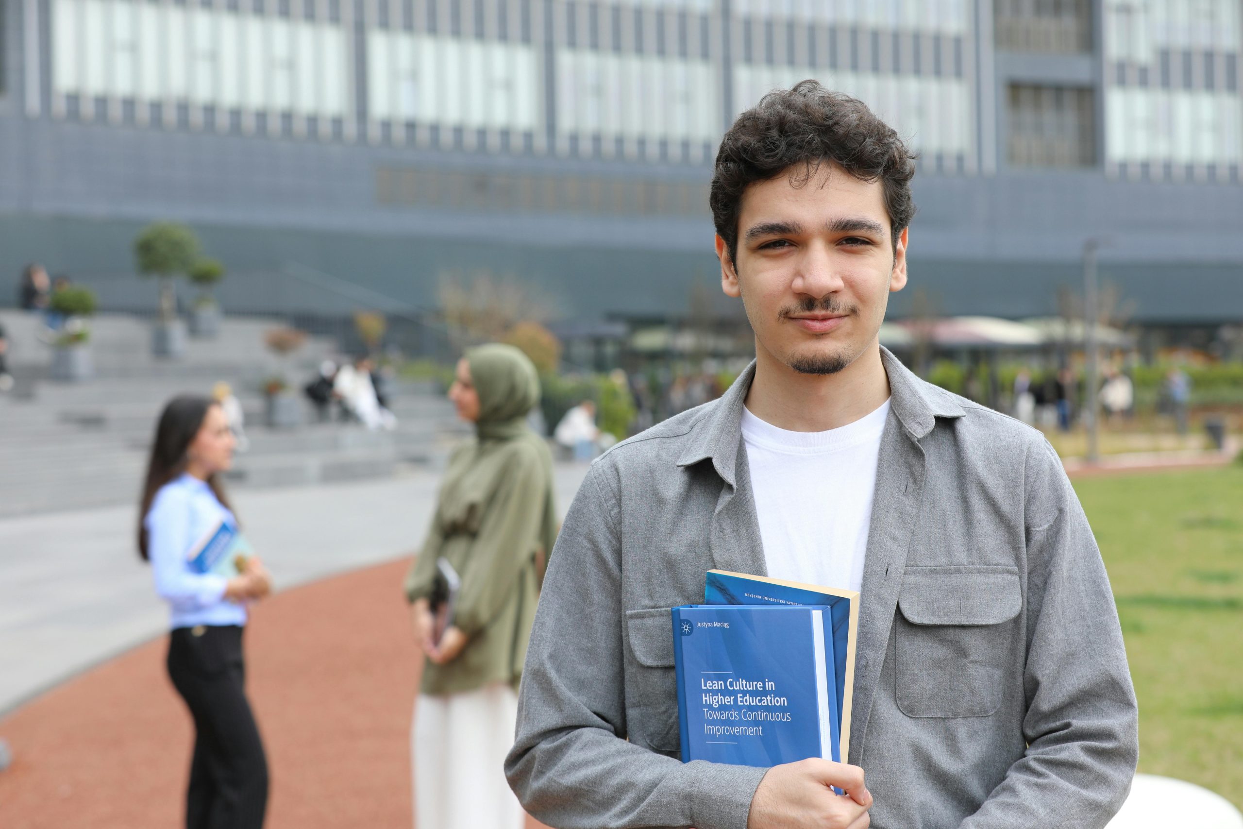 A young adult student stands outside on campus holding textbooks, symbolizing education.